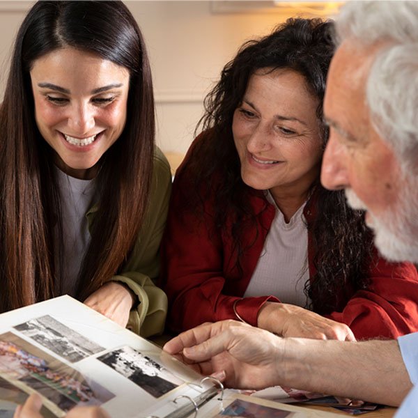 A woman, a man, and a senior woman joyfully looking through a photo album together.